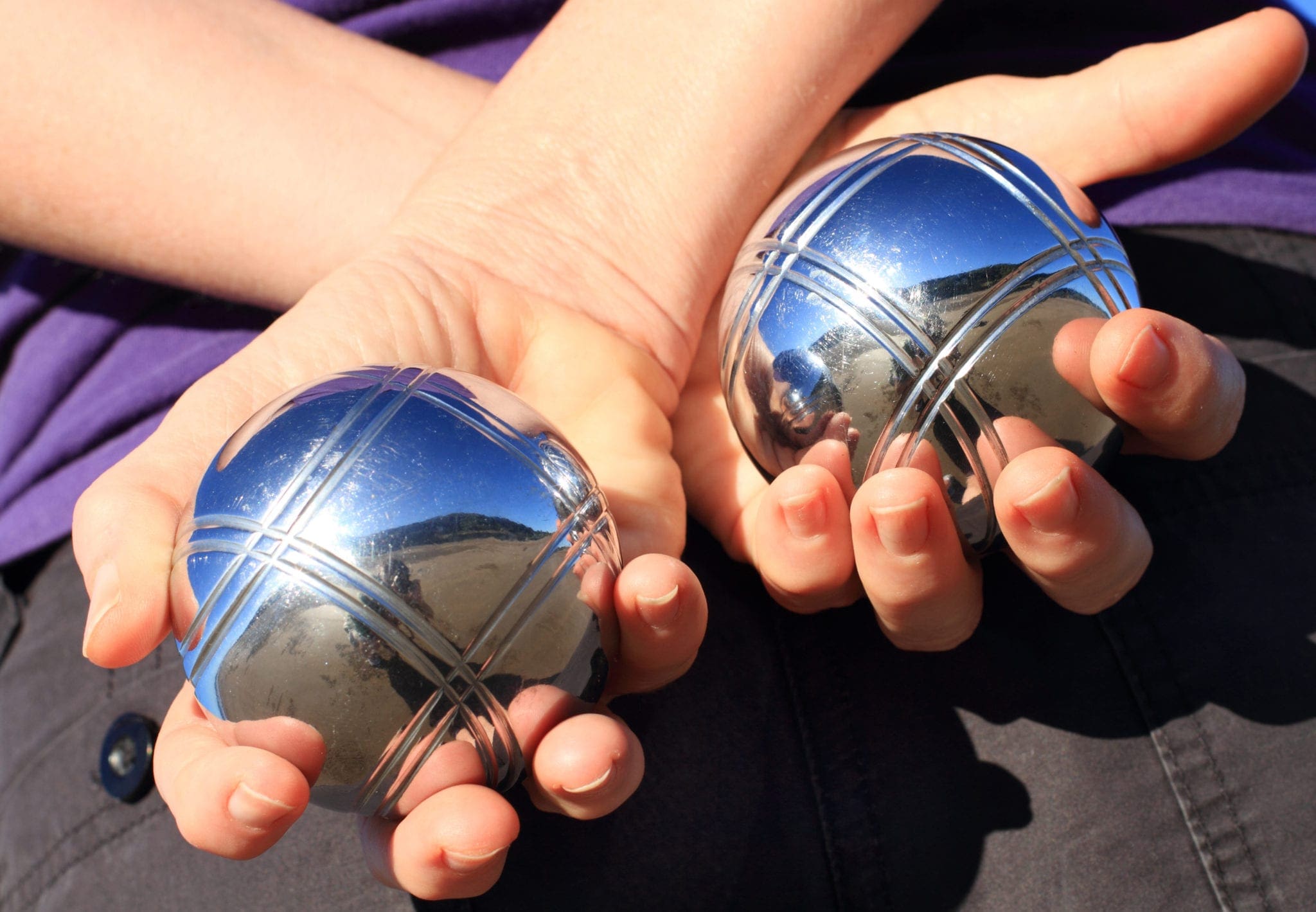 A woman holding two chrome boules behind her back.